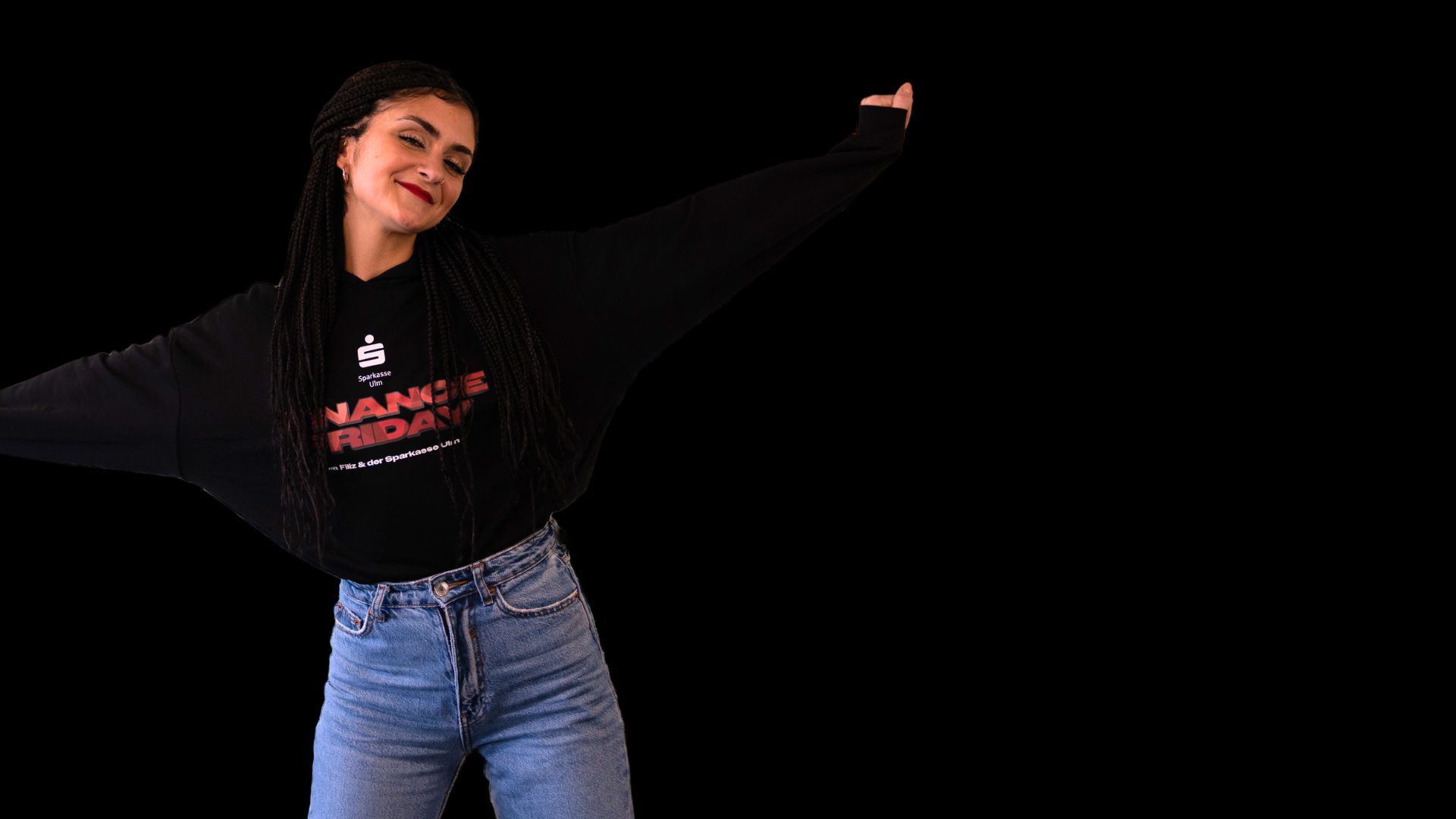 bigFM-Moderatorin Filiz vor schwarzem Hintergrund in Jeans und schwarzem Pullover