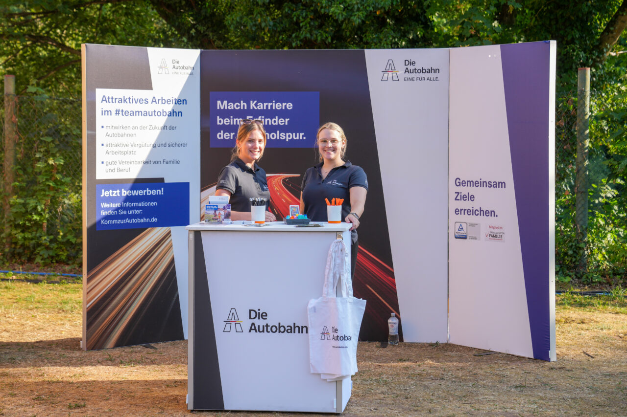 Zwei junge Promotiondamen stehen an einem Messestand vor einer Klappwand