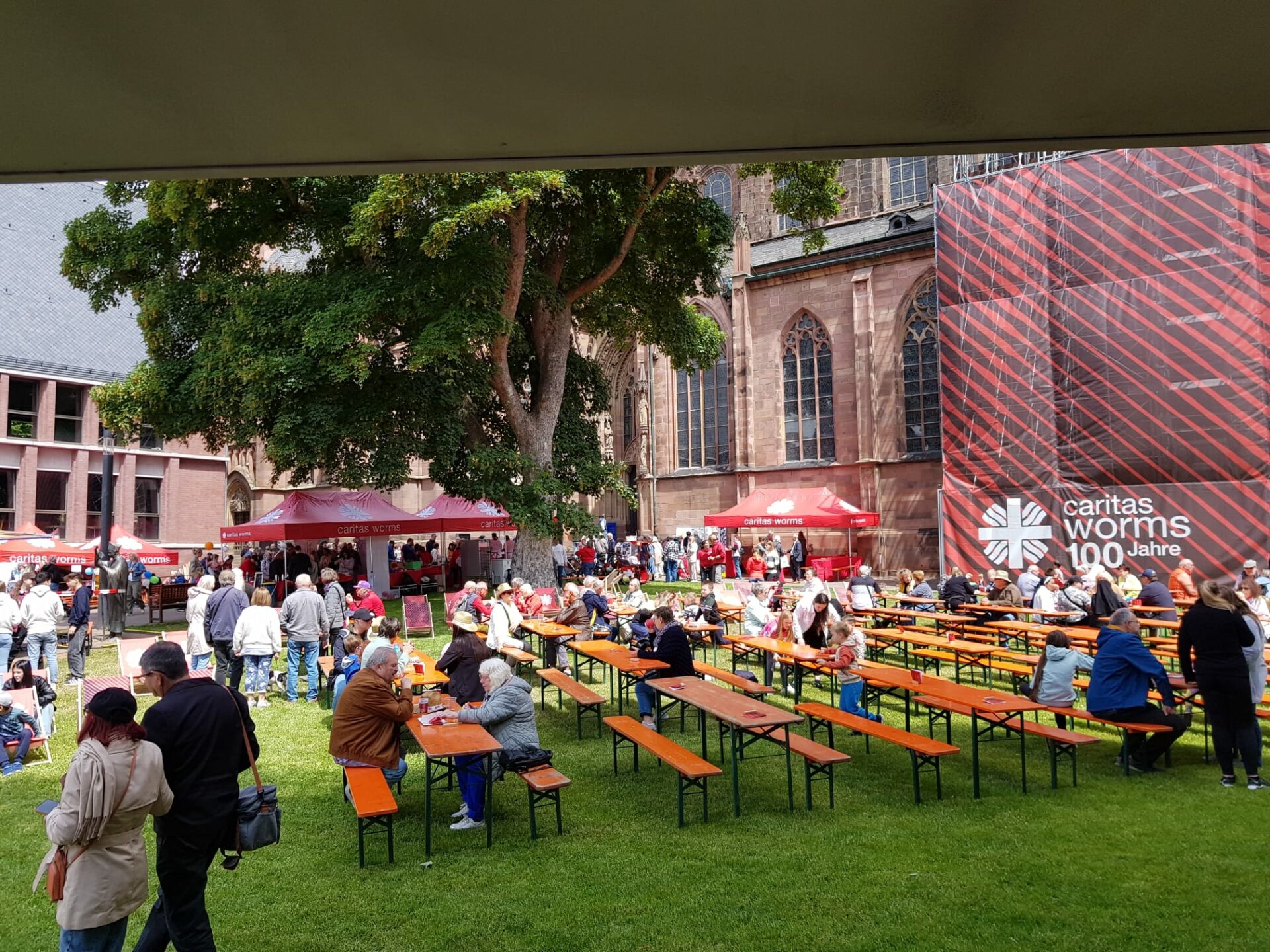 Besucher sitzen an Bierzeltgarnituren auf der Festwiese vor dem Wormser Dom